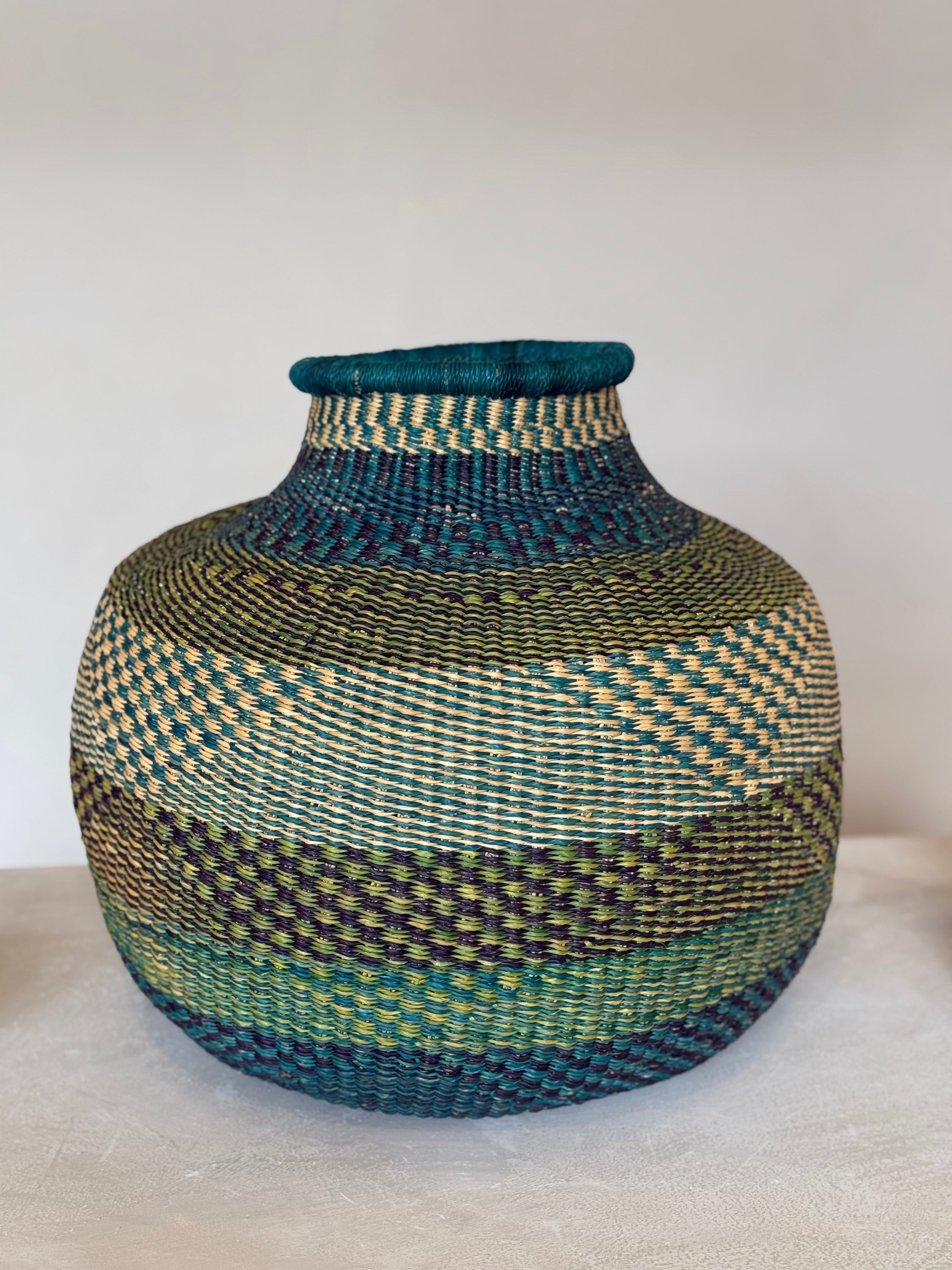 Large handwoven Ghanaian basket in teal, green and natural tones, shown upright on a neutral surface.