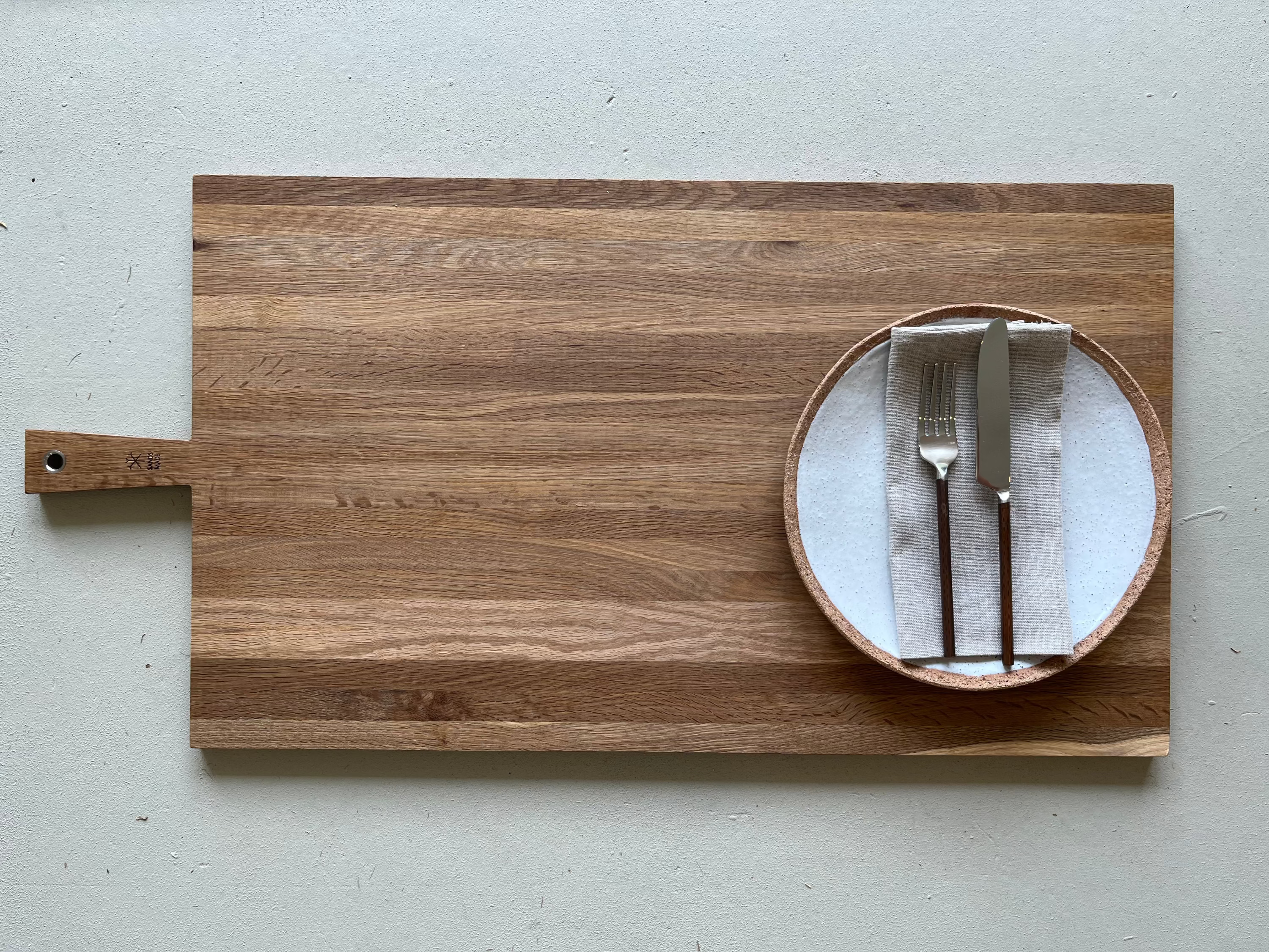 Wooden cutting board with a plate of cutlery on a light gray background