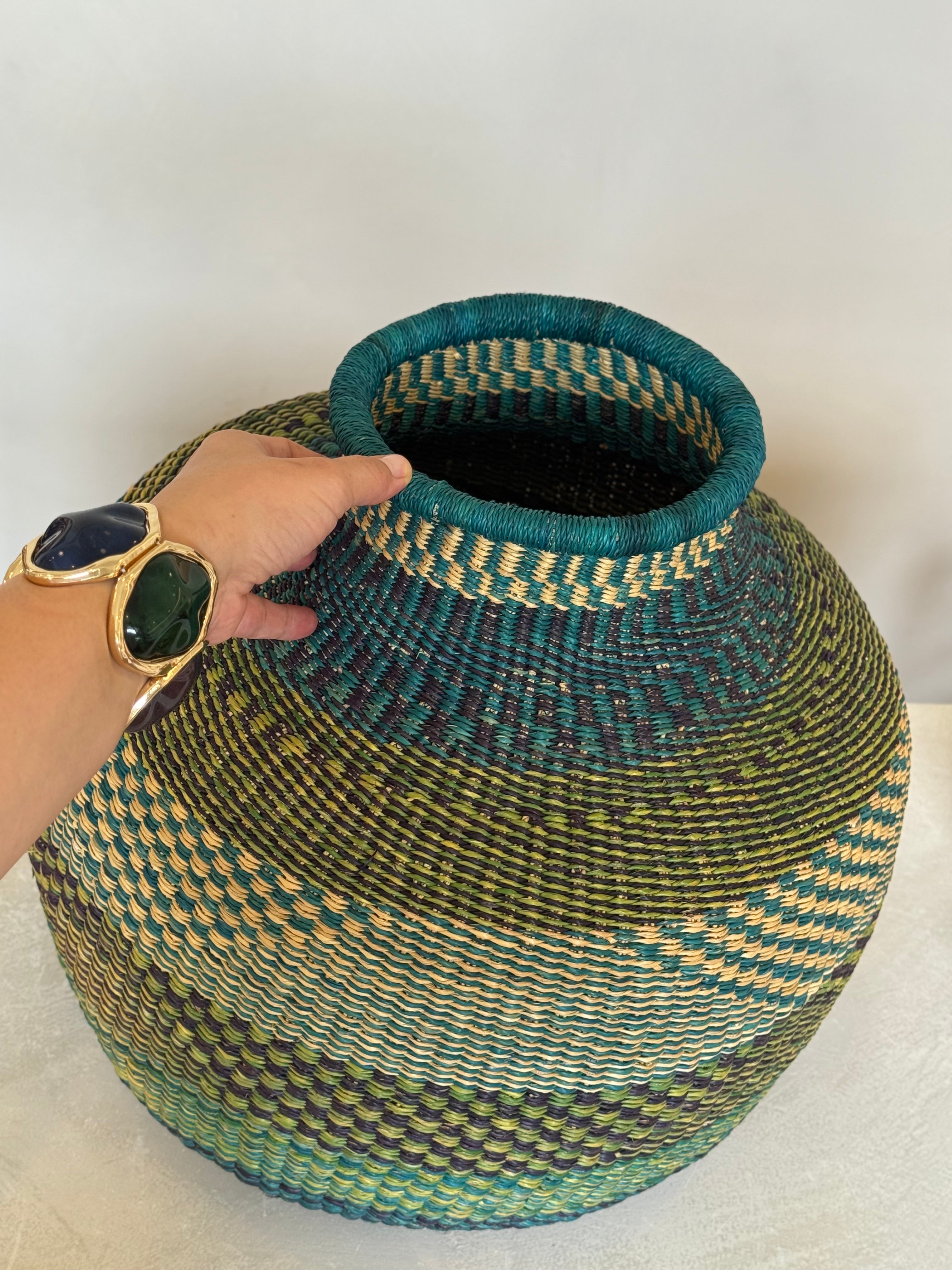Person holding the rim of a teal and green woven basket, showing texture and scale.