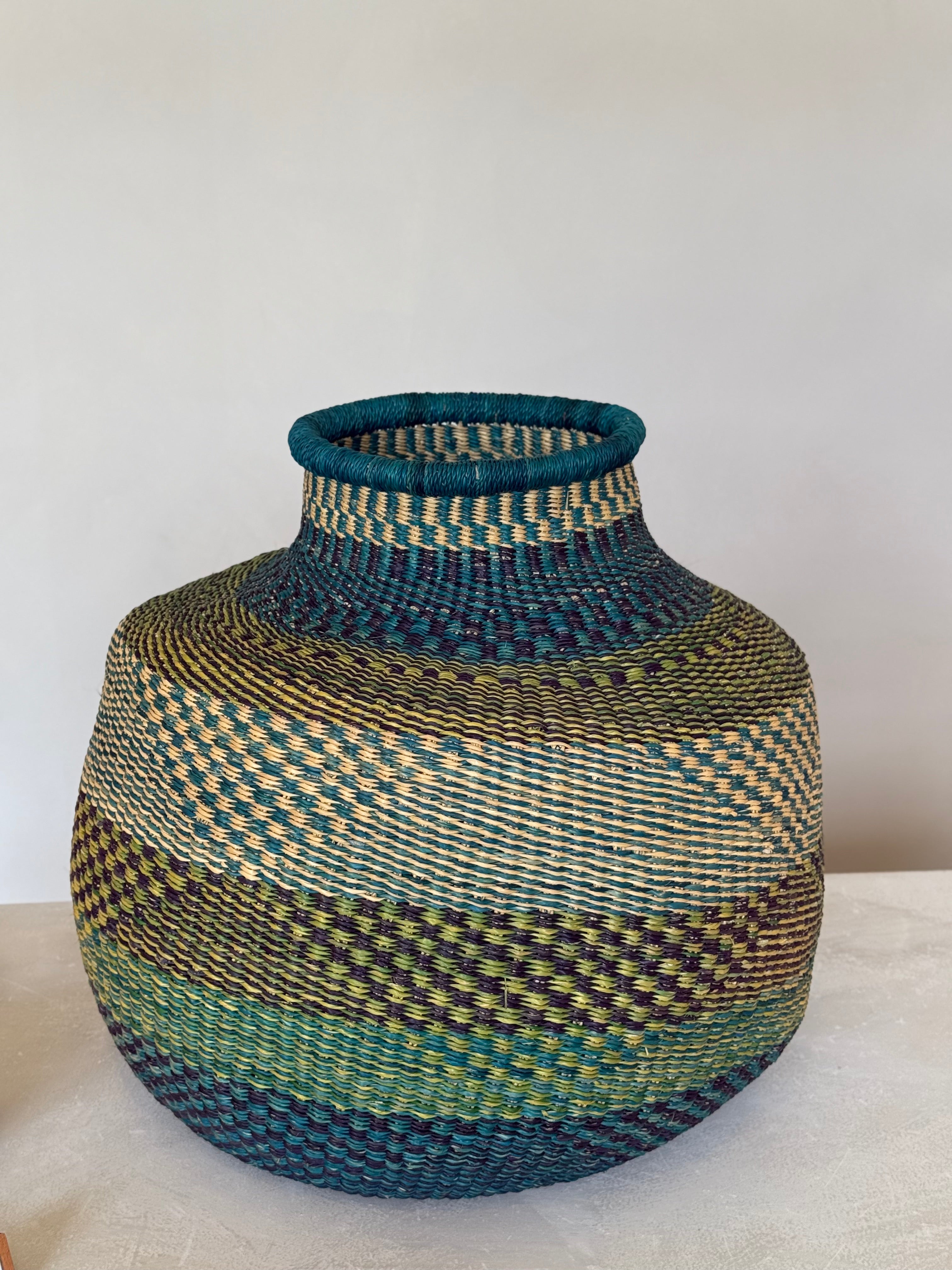 Side view of teal and green Ghanaian basket with detailed woven pattern in layered tones.